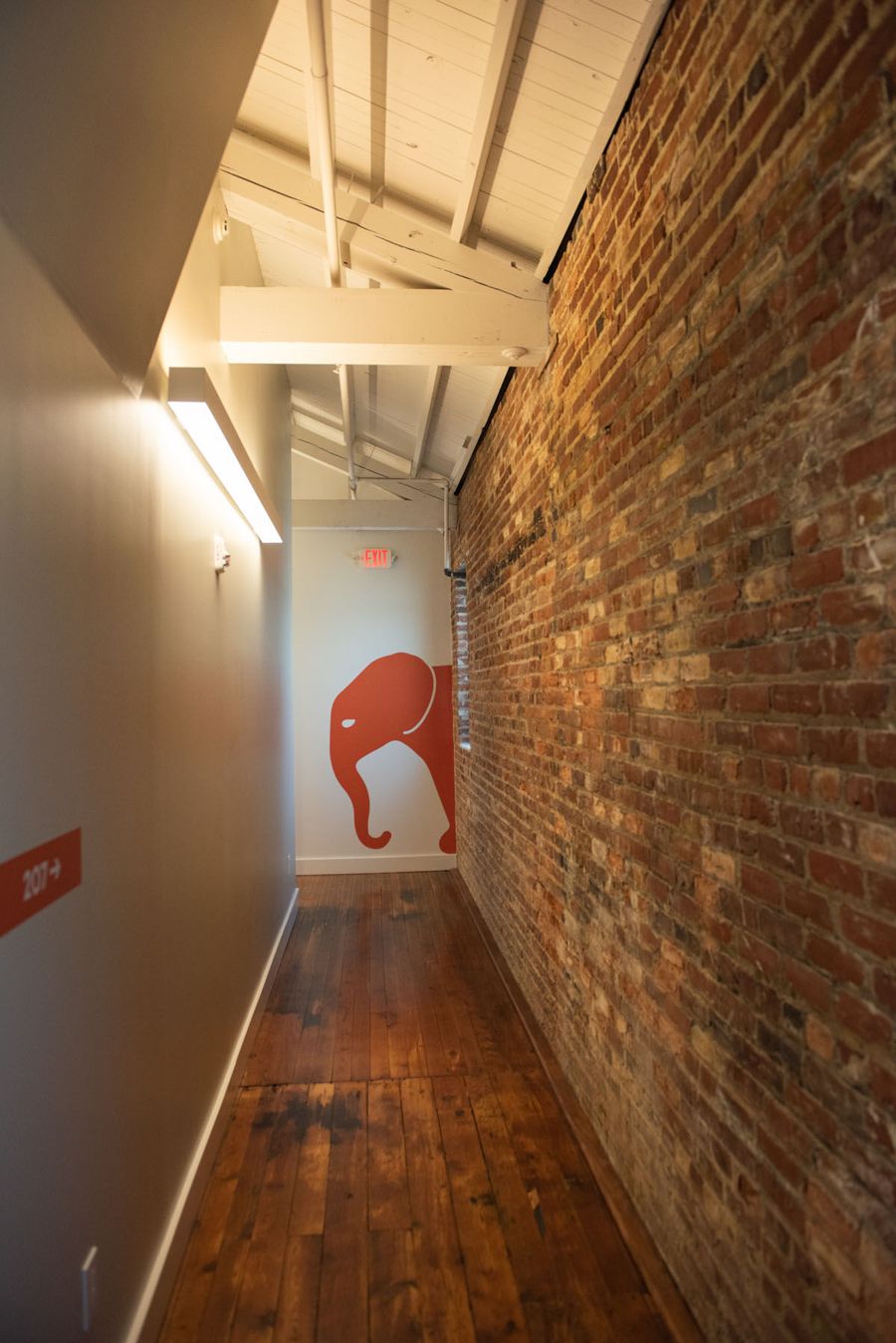 Long corridor beside an exposed brick wall, ending in an orange VANTAGE elephant painted on the wall