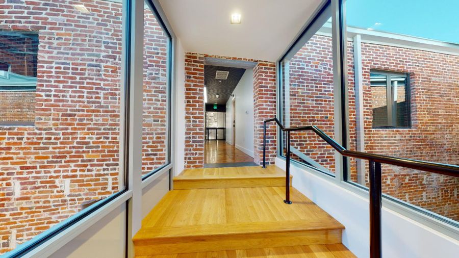Inside the glass-walled bridge connecting the two buildings, with steps leading up between exposed brick walls
