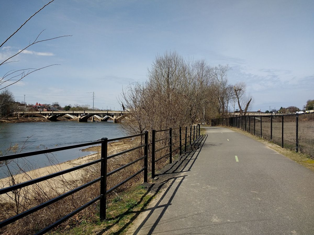 The paved Riverwalk Trail running beside the Dan River, with an arched bridge and downtown Danville in the distance