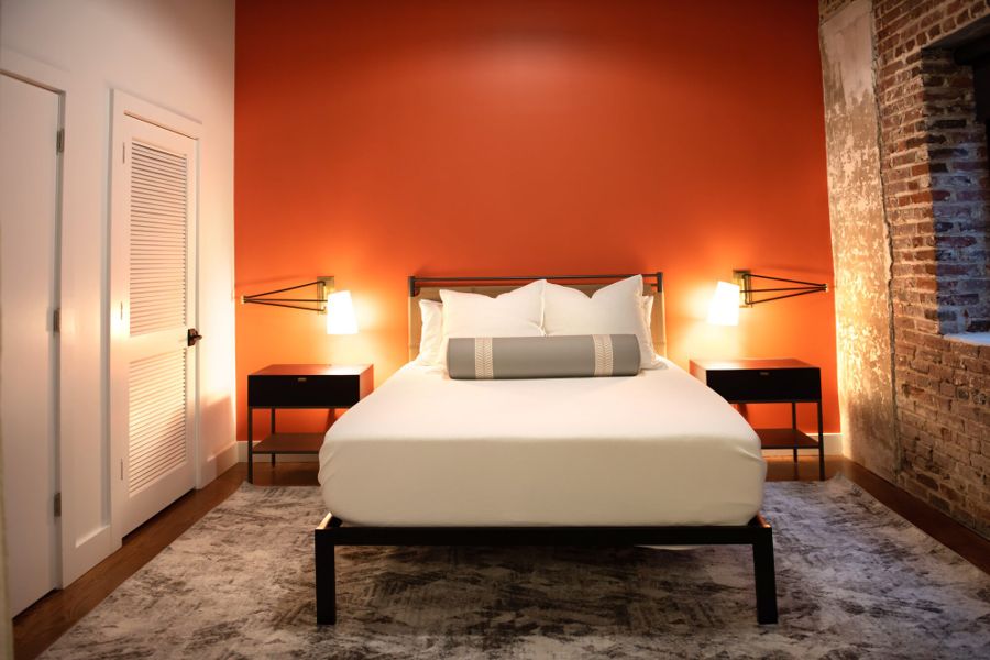 Bedroom with an orange feature wall, brass swing-arm lamps and exposed brick