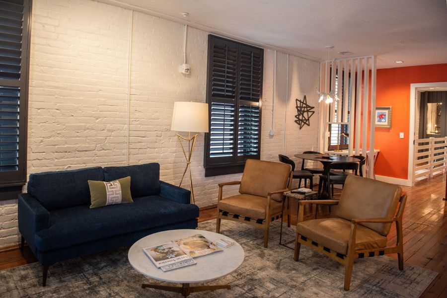 Living room with a navy sofa and leather armchairs, white brick walls and an orange accent wall beyond