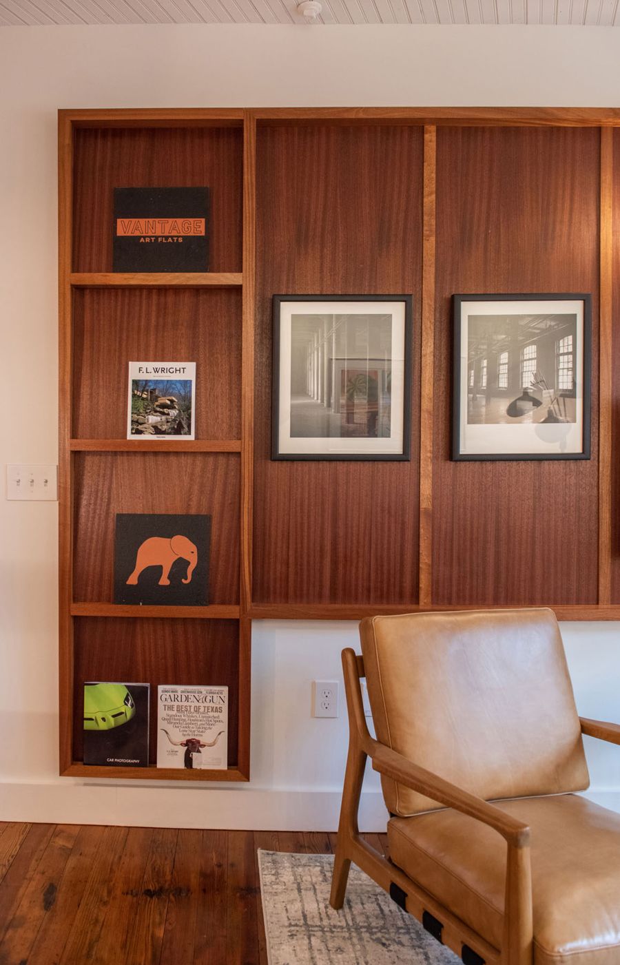 Sapele wood built-in shelves with art books, framed black-and-white photographs and a leather armchair