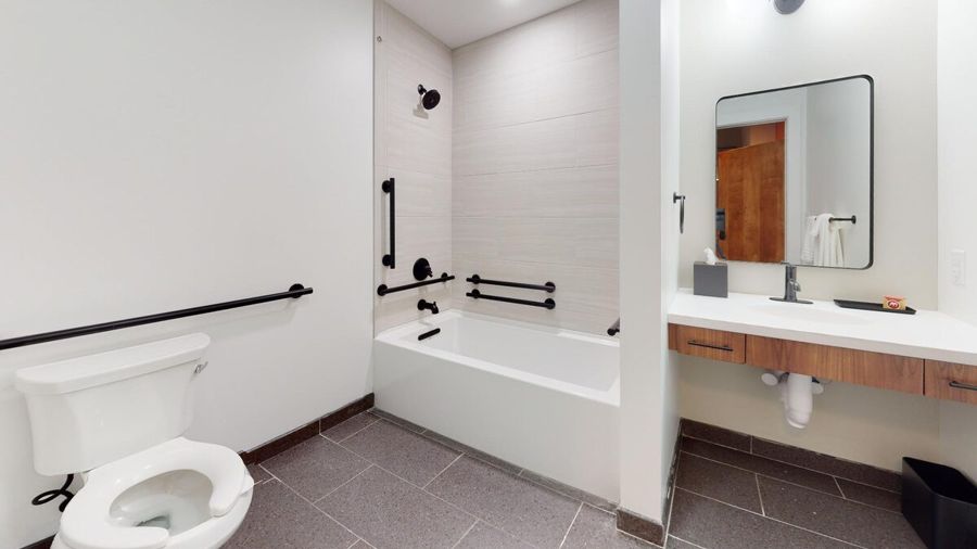 Bathroom with a tiled tub and shower, grab bars and a floating sapele vanity