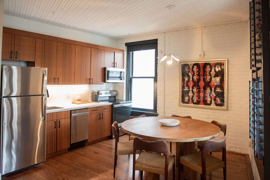 Kitchen with sapele wood cabinetry and stainless steel appliances beside a round dining table with woven-seat chairs