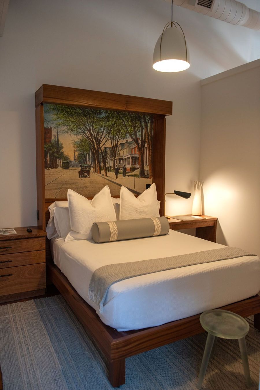 Bedroom with the vintage street postcard headboard, a white pendant light and a sculptural stool