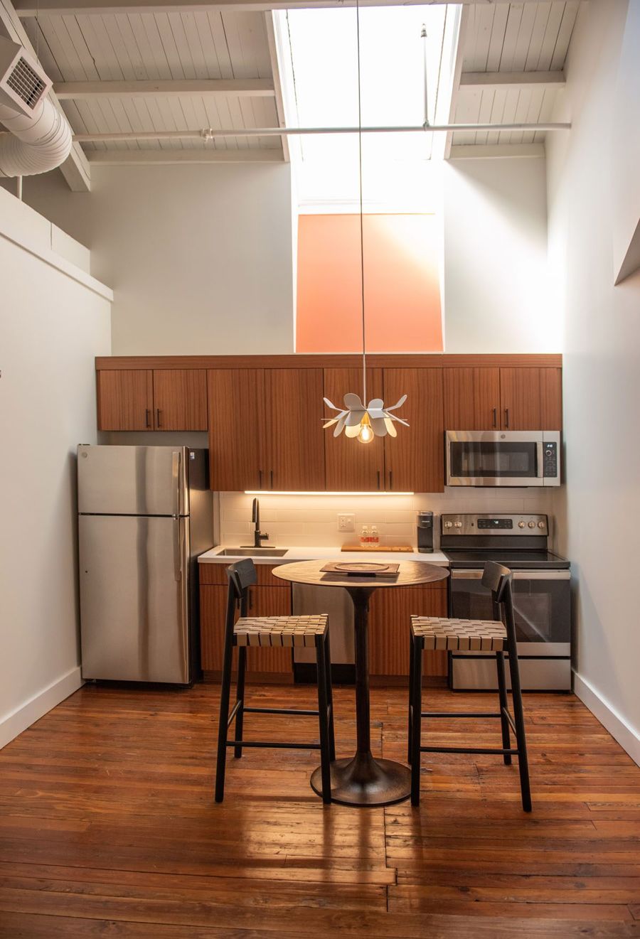 Eat-in kitchen with sapele wood cabinetry and a round bistro table beneath a soaring skylight shaft painted brand orange