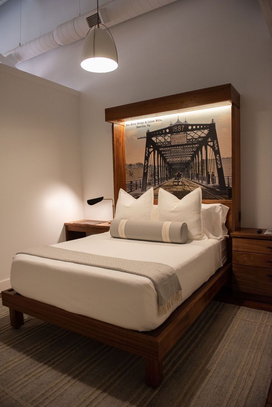 Bedroom with a sapele bed frame and backlit headboard framing a vintage postcard of the 1887 Dan River Bridge