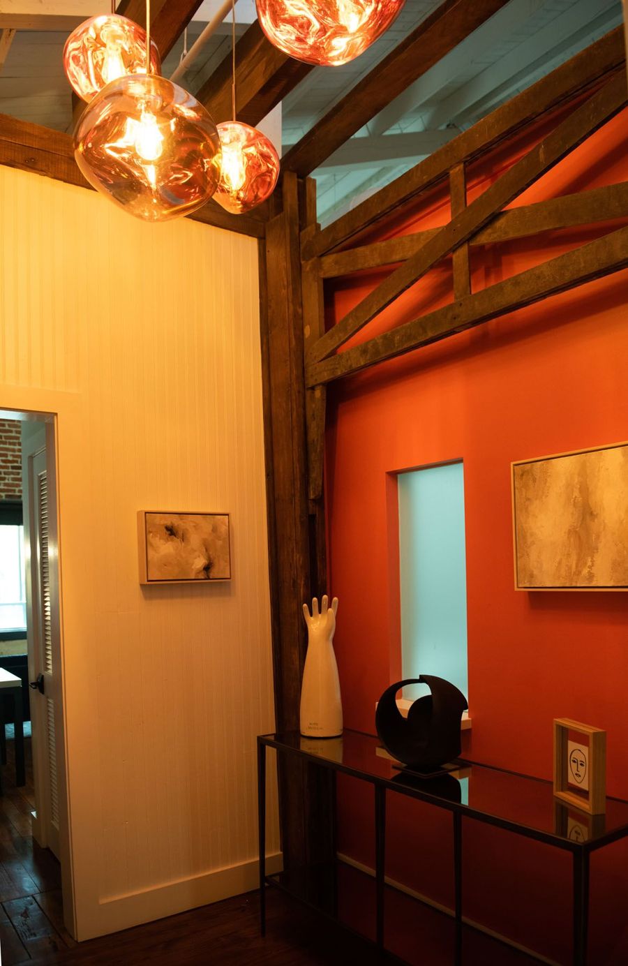 Entry with copper glass pendant lights hanging from exposed timber beams beside an orange accent wall and console table