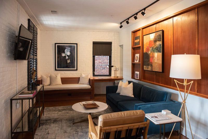 Living room with a blue velvet sofa, leather armchair, built-in window bench, sapele wood gallery wall and white brick walls