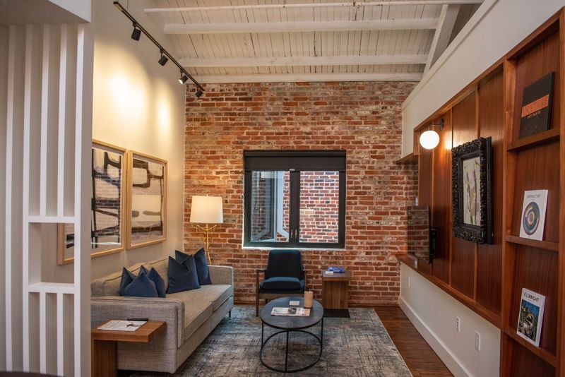 Living room with a grey sofa, navy pillows, abstract black-and-white prints and a sapele wood built-in wall facing an exposed brick wall